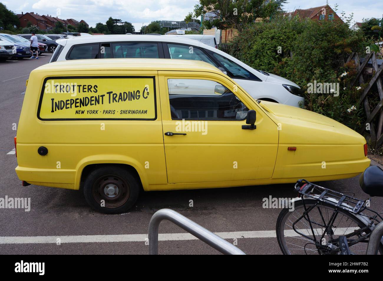 Seitenansicht des Yellow Reliant Robin 3 Wheeler Van auf einem Parkplatz mit Trotter`s Independent Trading auf der Seite Stockfoto